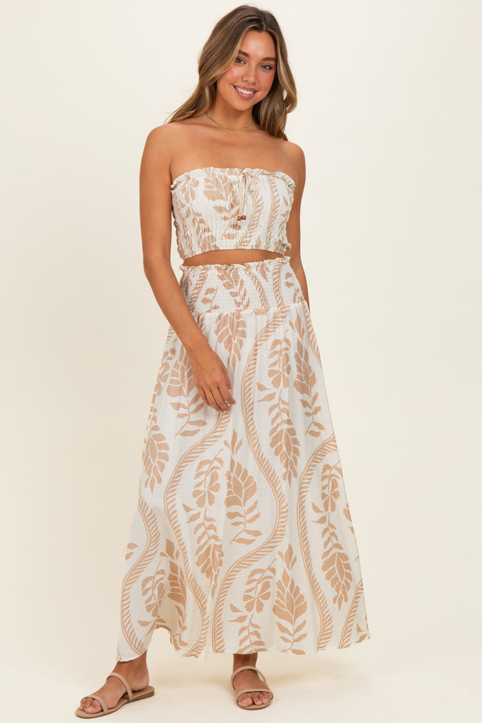 woman wearing a strapless crop top and matching maxi skirt with beige leaf patterns