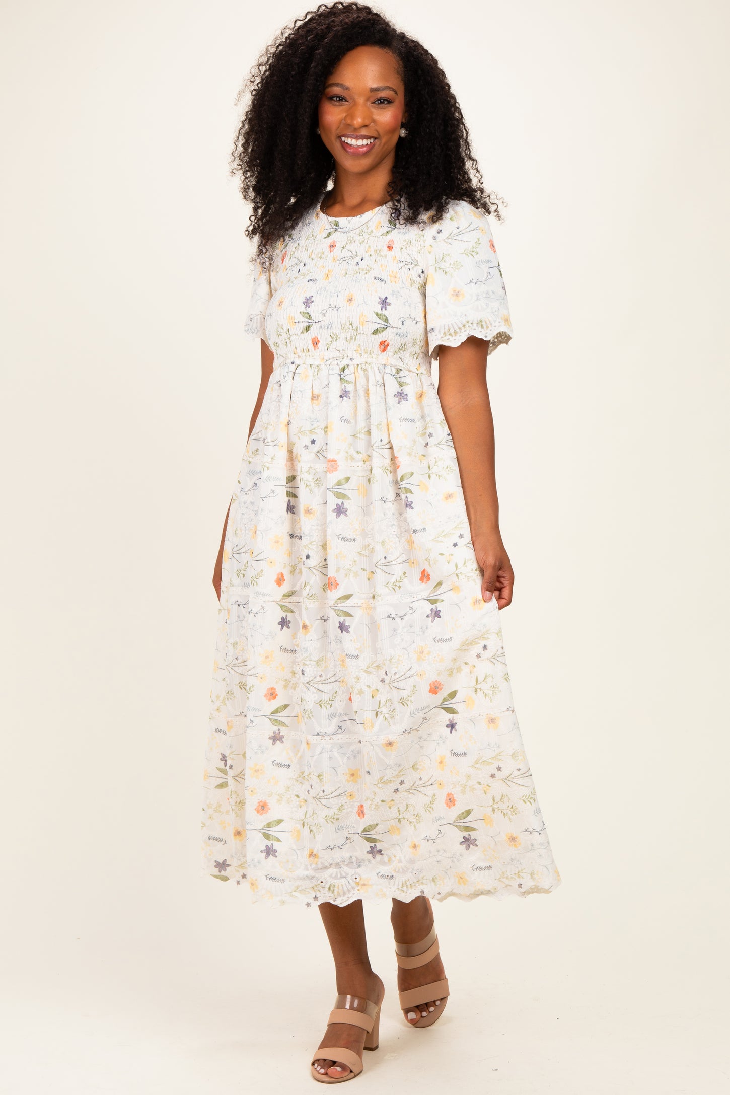 woman wearing a white floral midi dress with short puff sleeves and a gathered waist, smiling at the camera