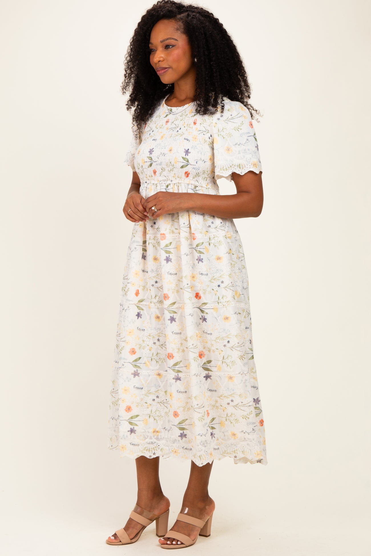 woman wearing a white floral midi dress with short sleeves and lace detailing, standing in a neutral background