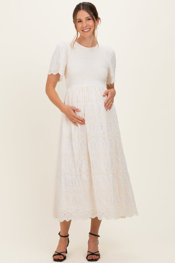 woman wearing a white lace maternity dress with short sleeves and a flowy skirt, gently holding her baby bump