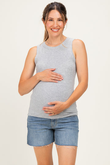 woman wearing a light gray maternity tank top and holding her baby bump while smiling, paired with denim shorts