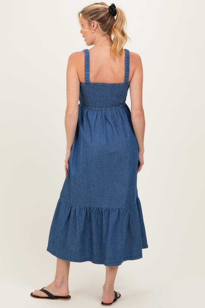 woman wearing a denim blue maternity maxi dress with smocked bodice and tiered ruffle hem, showing her baby bump from the back