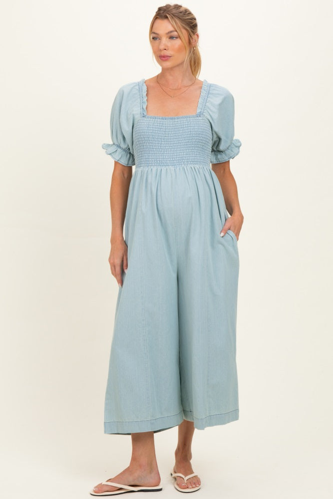 woman wearing a light blue maternity jumpsuit with puff sleeves and a fitted bodice, holding her baby bump