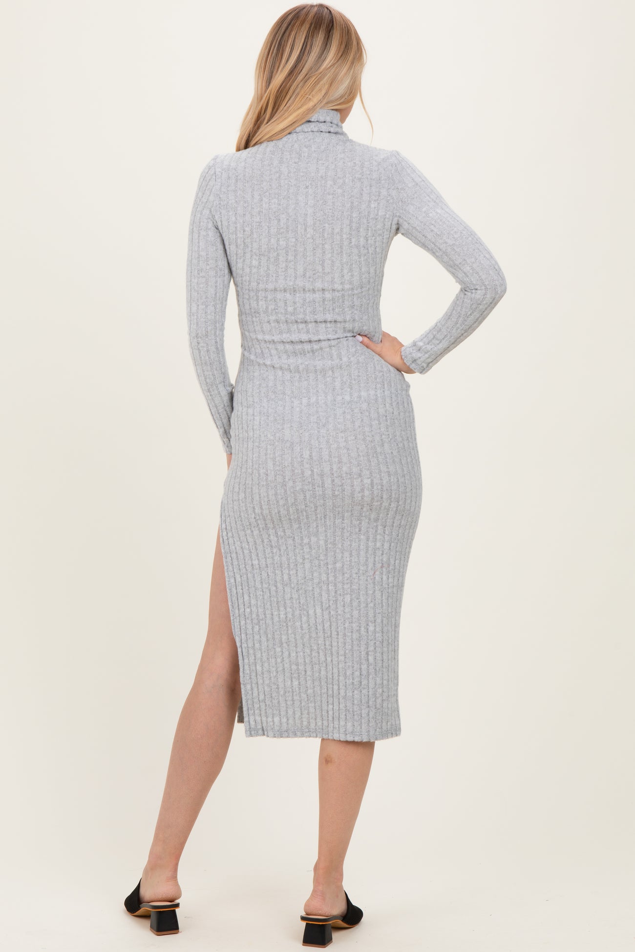 woman wearing a fitted gray ribbed midi dress with a high slit and long sleeves, showing the back view