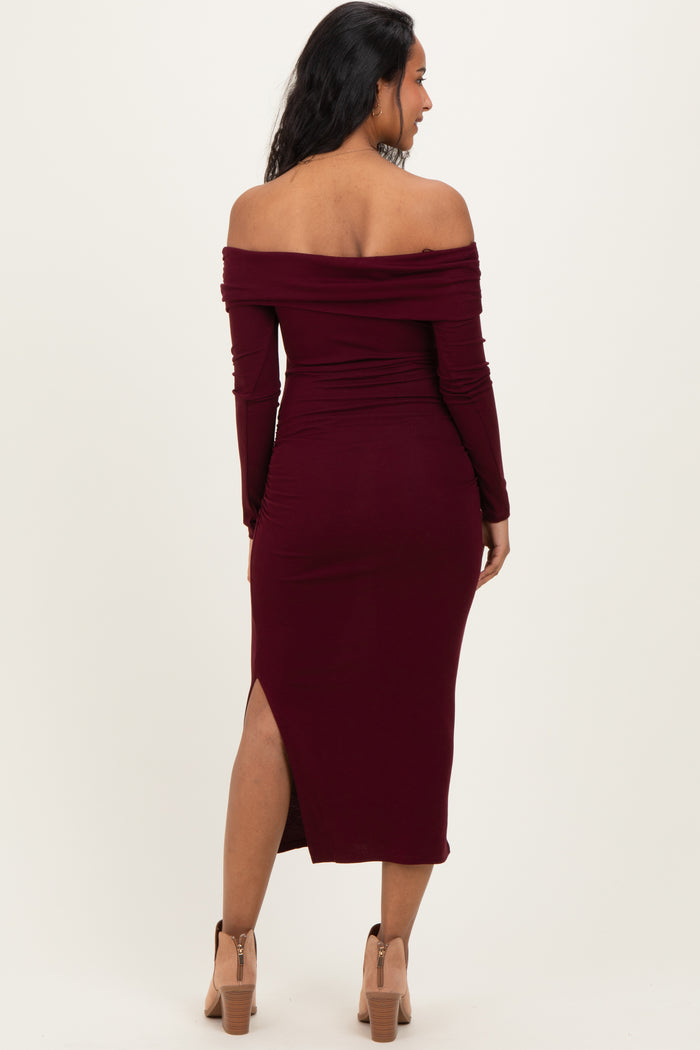 woman wearing a burgundy off-the-shoulder maternity dress with long sleeves and a thigh-high slit, showing her baby bump