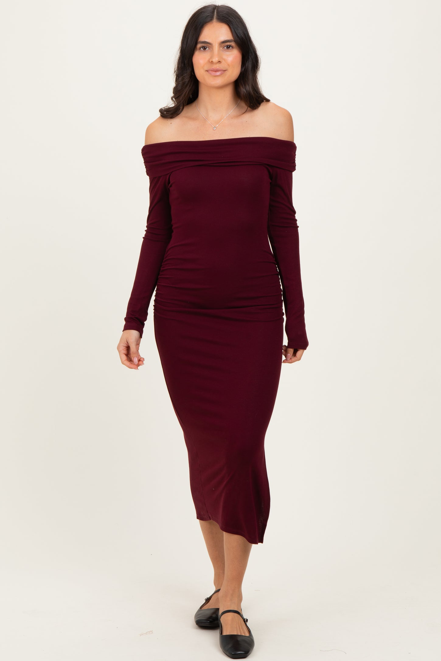woman wearing a burgundy off-the-shoulder midi dress with long sleeves and a fitted silhouette
