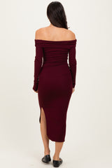 woman wearing a burgundy off-the-shoulder long sleeve dress with a side slit and form-fitting silhouette