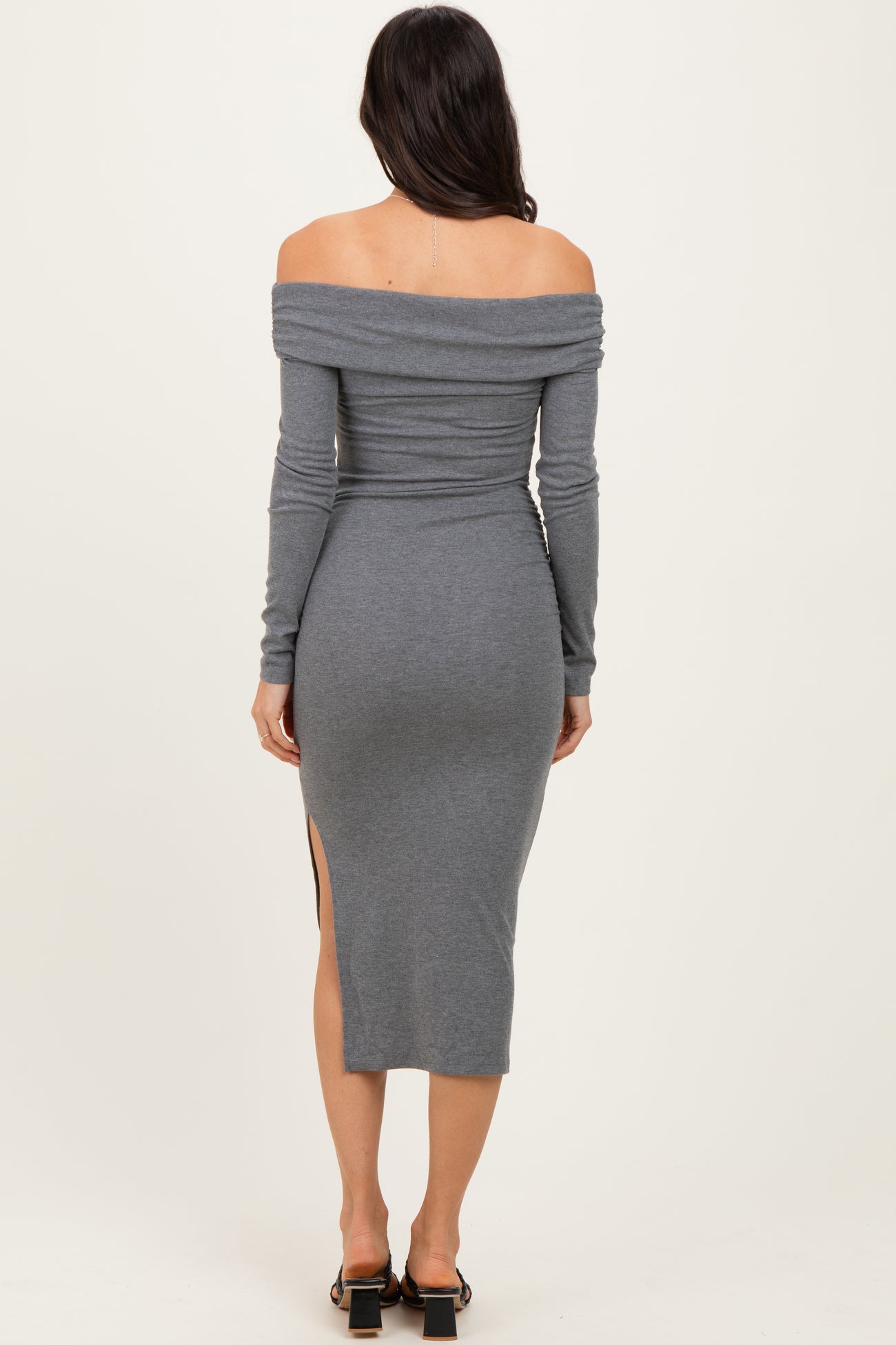 woman wearing a gray off-the-shoulder long sleeve dress with a thigh-high slit, viewed from the back