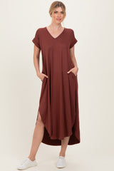 woman wearing a rust-colored v-neck short sleeve maxi dress with pockets and high-low hem, standing in white sneakers