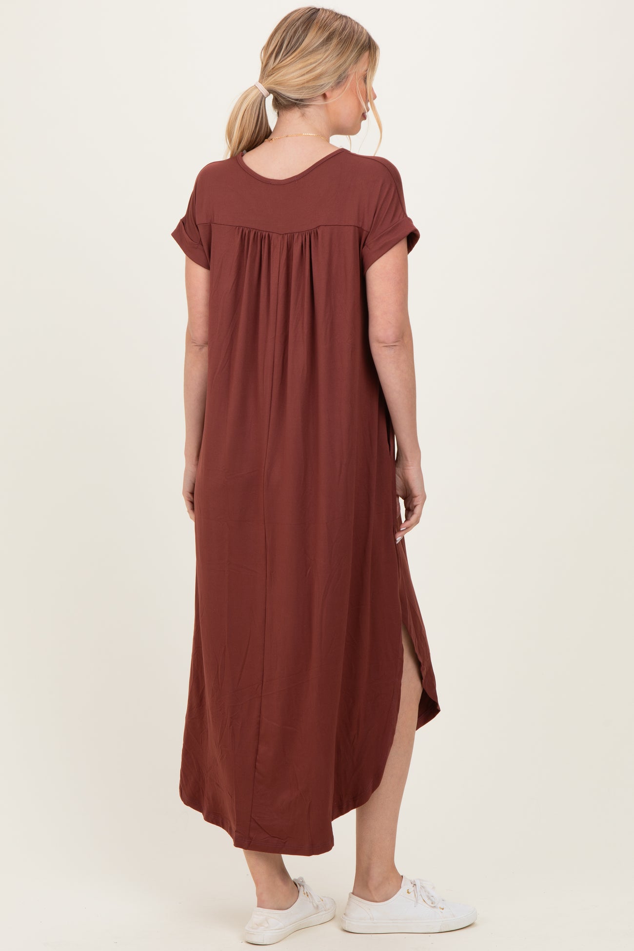 woman wearing a rust-colored maxi dress with short sleeves and a relaxed fit, showing a side slit
