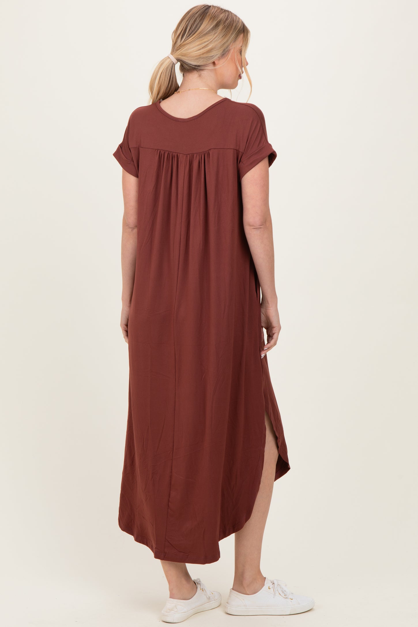 woman wearing a rust-colored maxi dress with short sleeves and a relaxed fit, showing a side slit