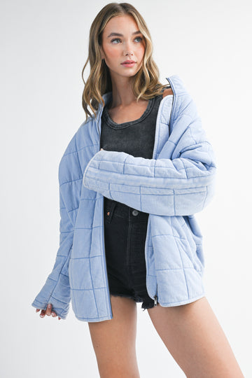 woman wearing a light blue quilted shacket over a black tank top and black denim shorts