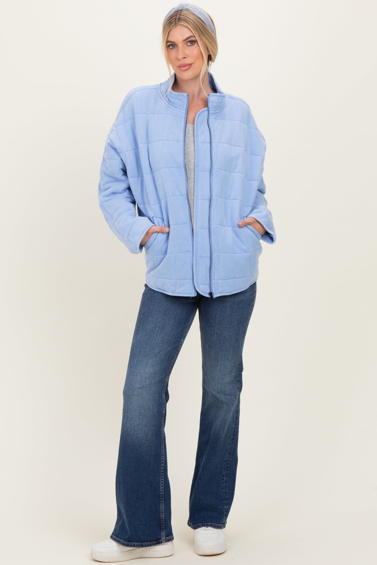 woman wearing a light blue quilted jacket with pockets, paired with a gray top and flared jeans