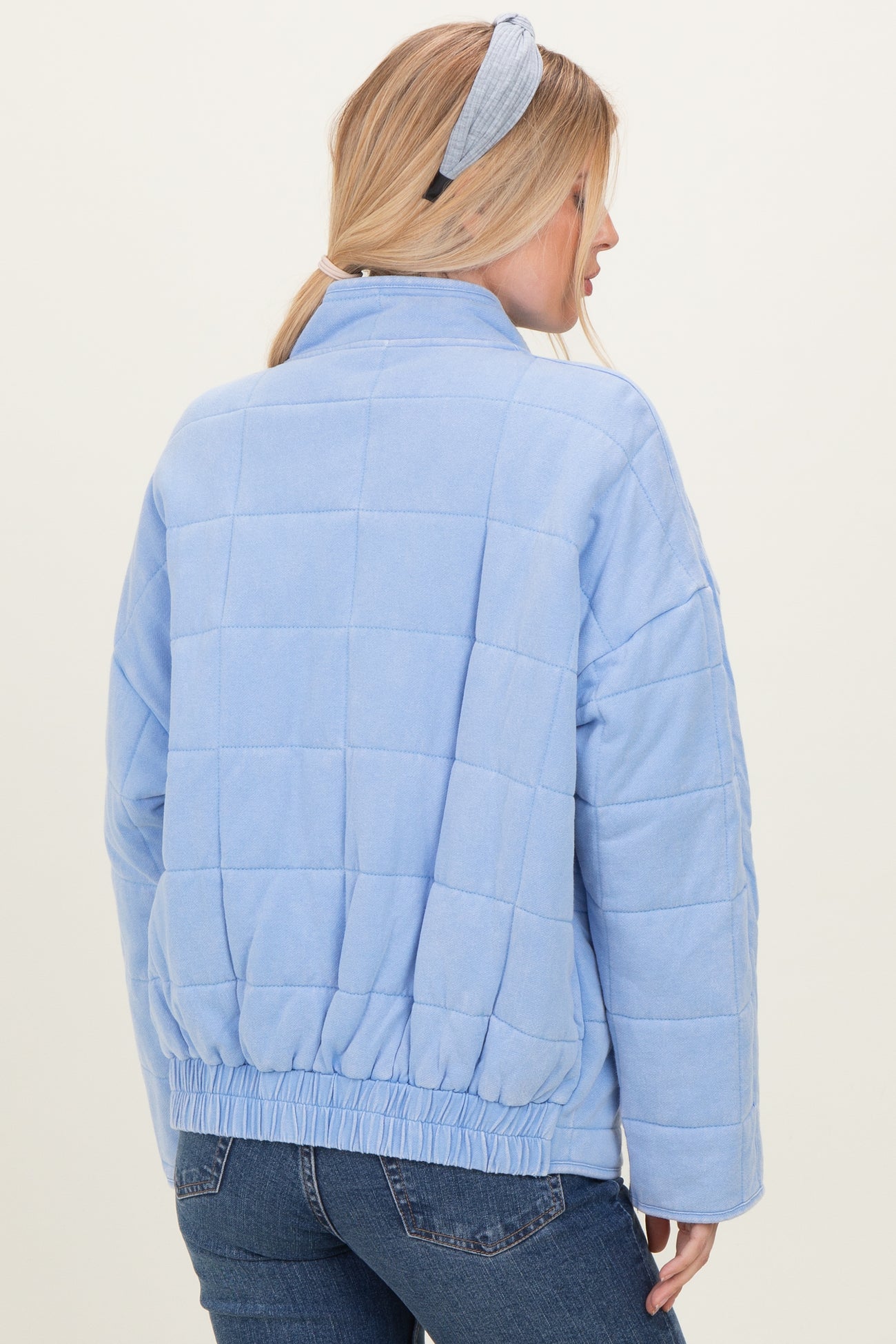 woman wearing a light blue quilted jacket with a cinched waist, styled with a matching headband, seen from the back