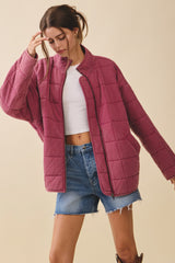 woman wearing a burgundy quilted jacket over a white crop top and denim shorts