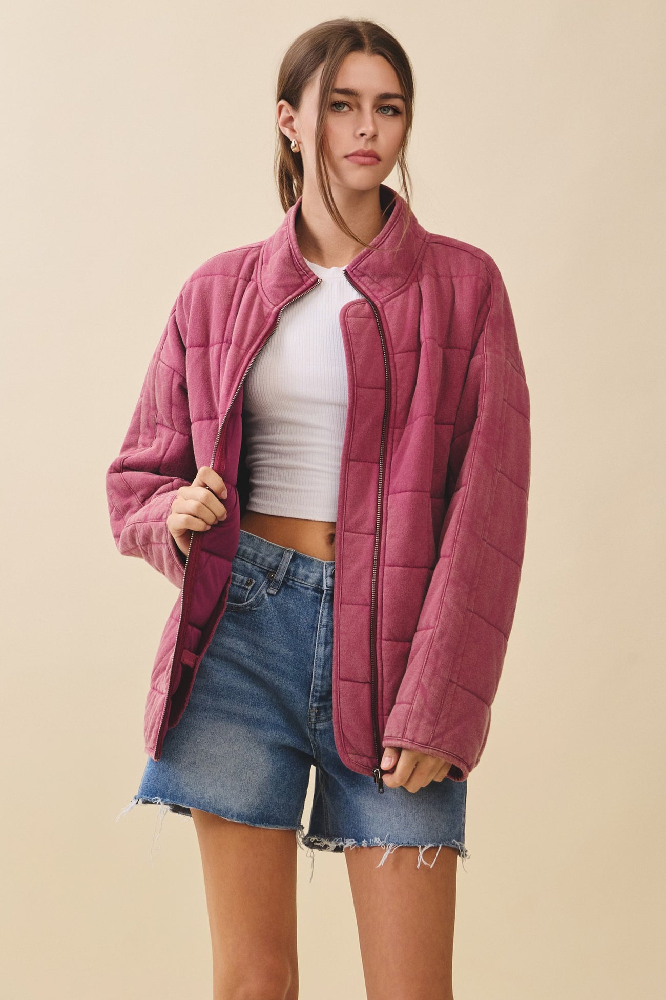 woman wearing a pink quilted jacket over a white crop top and denim shorts