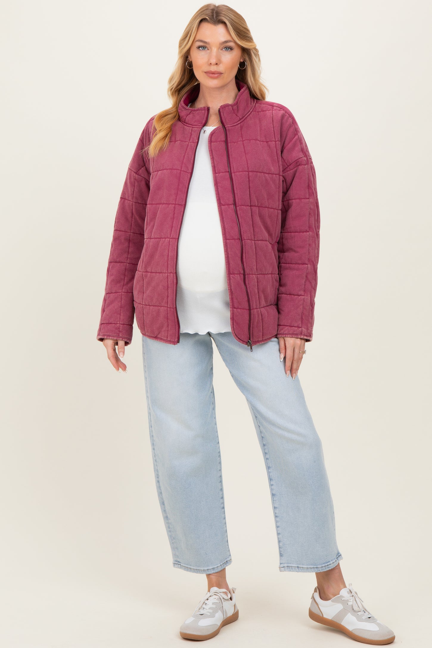 woman wearing a burgundy quilted maternity jacket over a white top and light blue jeans, showing her baby bump