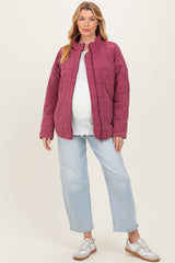 woman wearing a burgundy quilted maternity jacket over a white top and light blue jeans, showing her baby bump