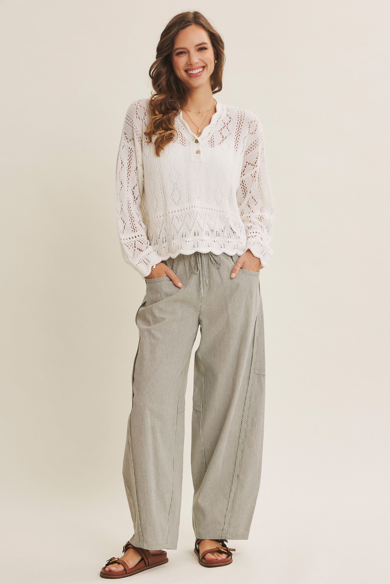 woman wearing a white long sleeve crochet top and gray striped wide-leg pants with pockets