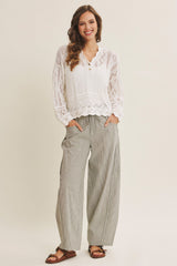 woman wearing a white long sleeve crochet top and gray striped wide-leg pants with pockets