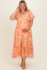 woman in a flowy peach floral maternity dress with puff sleeves and ruffled hem, gently holding her baby bump