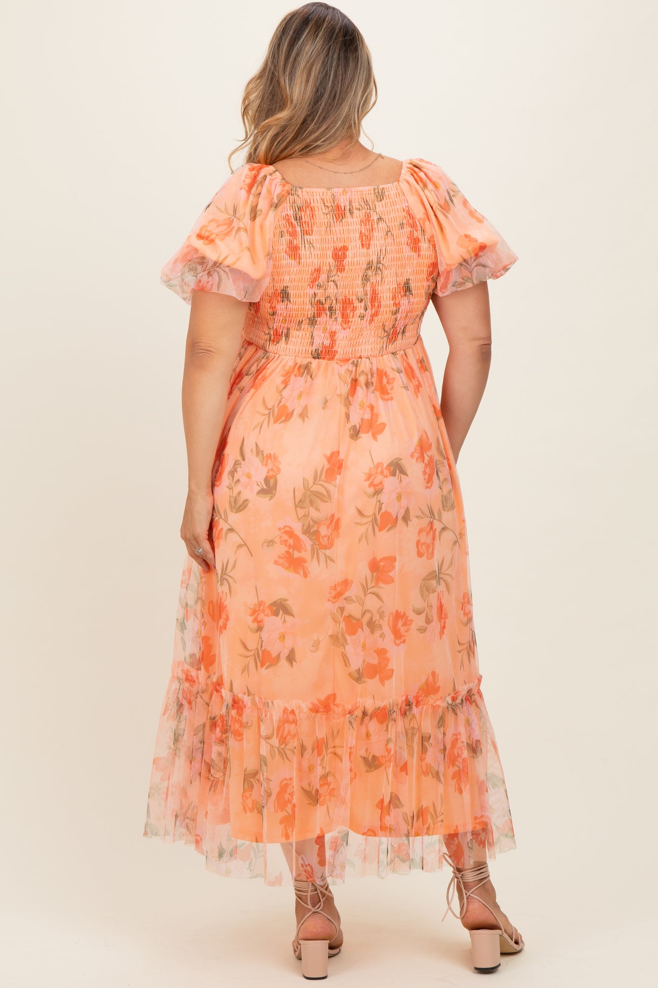 woman wearing a floral maternity plus dress in peach with puff sleeves and a tiered skirt, showing the back view
