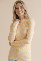 woman wearing a yellow long sleeve top with a floral pattern and a scalloped neckline
