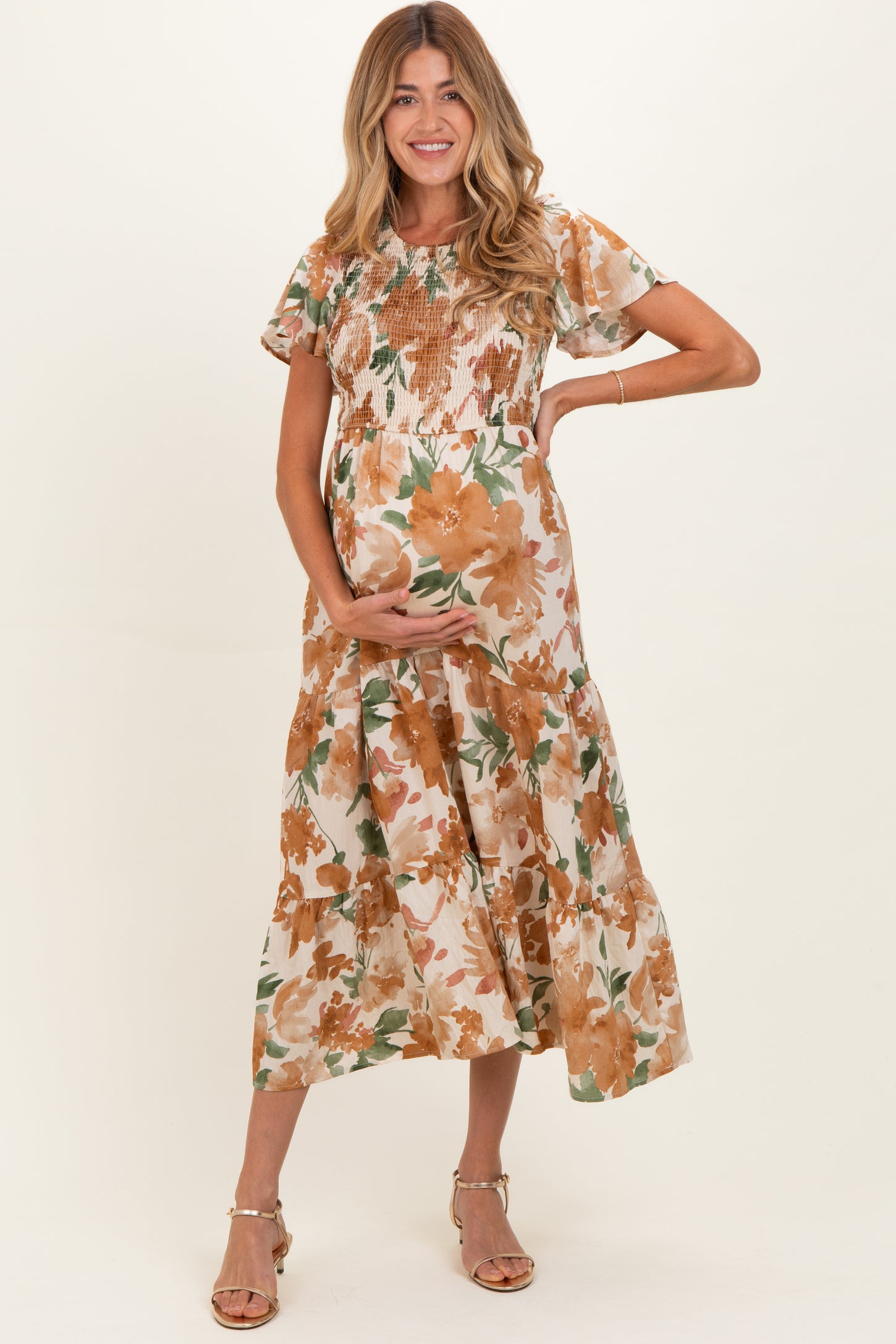 woman wearing a floral maternity dress with short sleeves and a tiered skirt, gently cradling her baby bump
