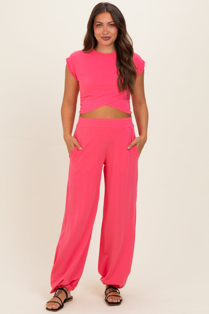 woman wearing a bright pink maternity two-piece set with a cropped top and loose-fitting pants, holding pockets