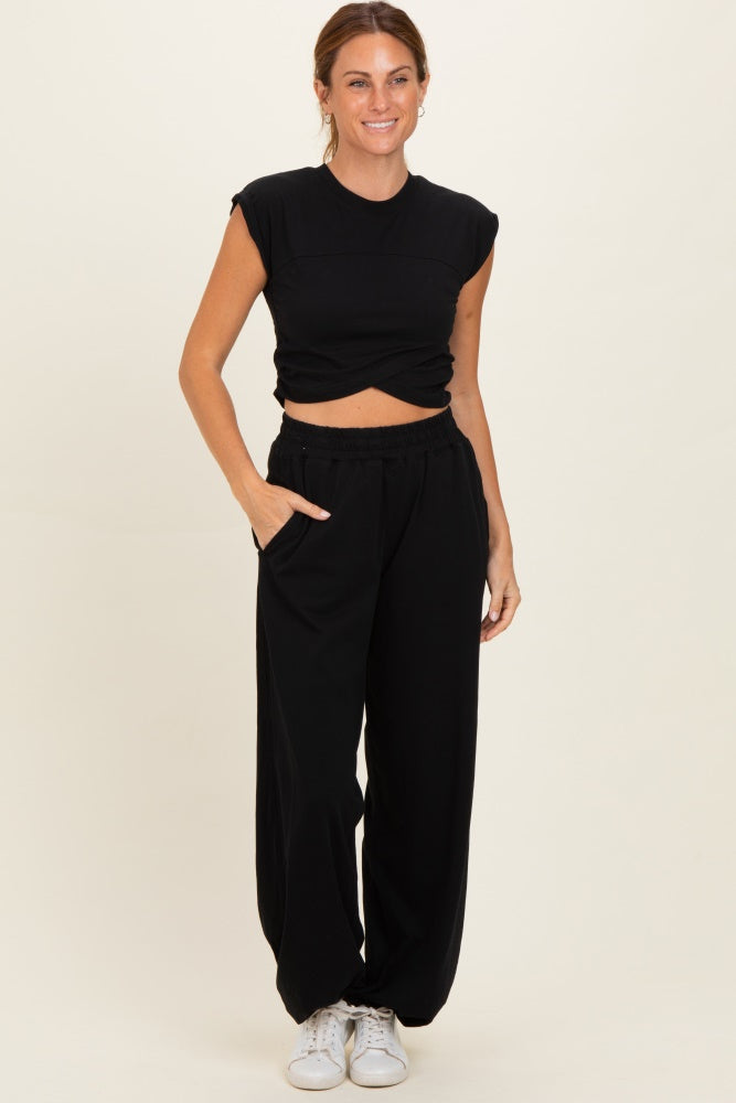 woman wearing a black sleeveless crop top and black wide-leg pants with pockets, styled with white sneakers