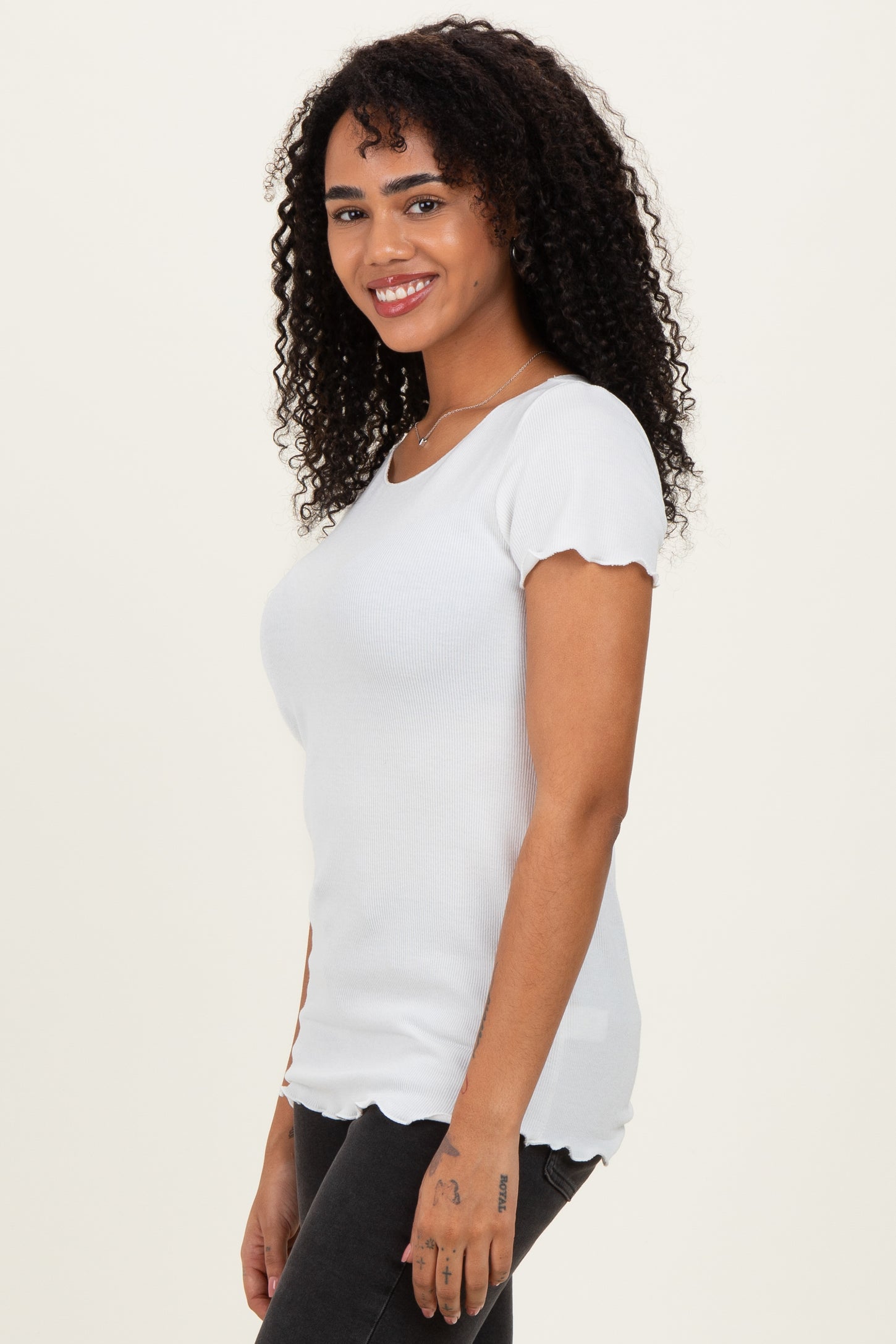 woman wearing a white ribbed top with scalloped sleeves and a fitted silhouette