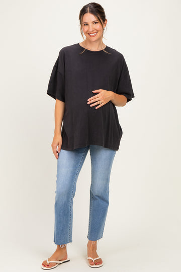 woman wearing a black oversized maternity top and light blue jeans, holding her baby bump