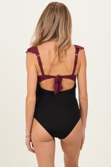 woman wearing a black maternity swimsuit with burgundy ruffle straps and a tied back detail