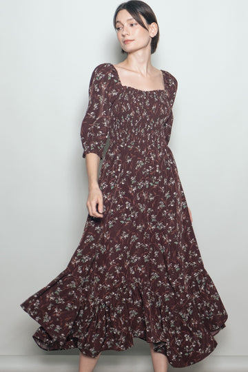 woman wearing a burgundy floral print maxi dress with puff sleeves and a ruffled hem