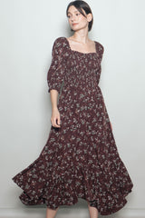 woman wearing a burgundy floral print maxi dress with puff sleeves and a ruffled hem