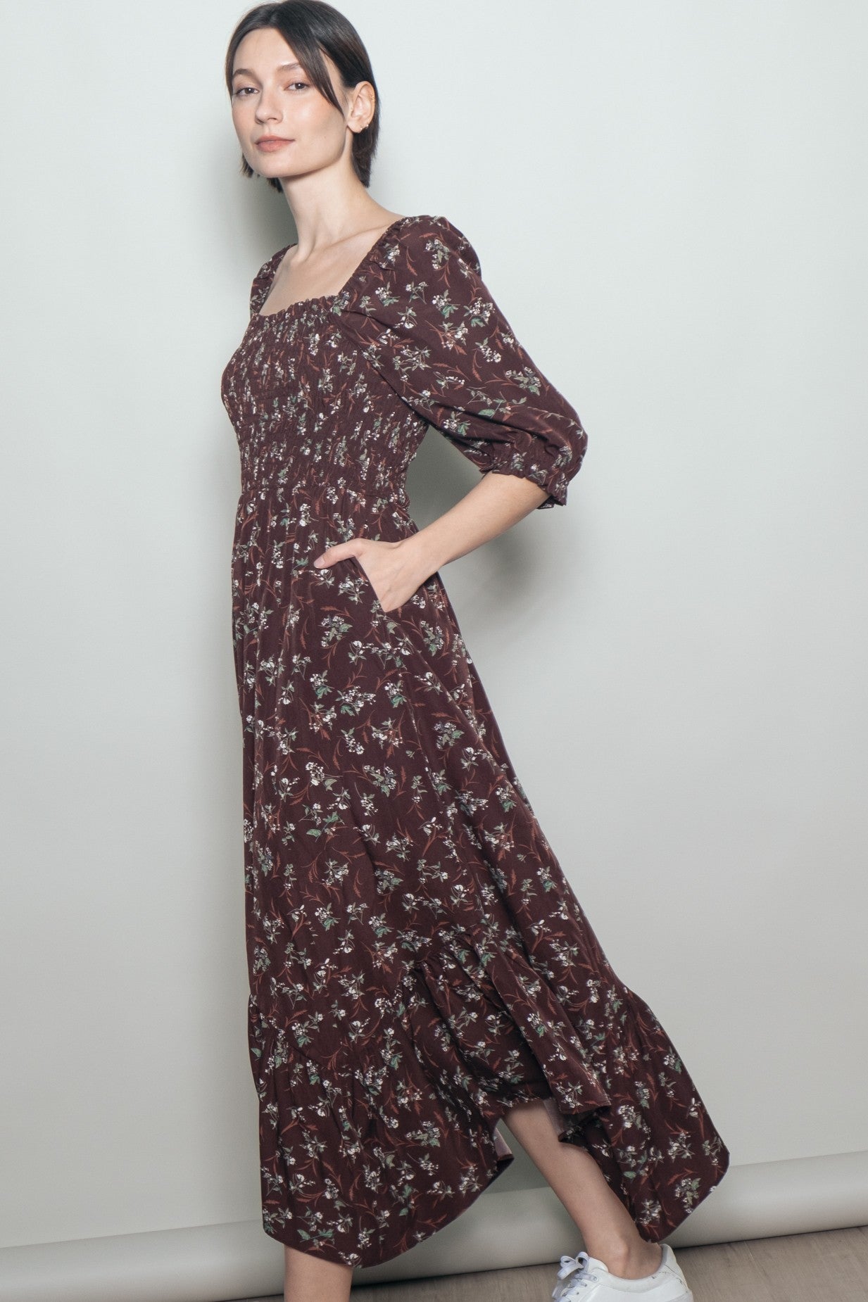 woman wearing a burgundy floral maxi dress with puff sleeves and pockets, standing against a light background