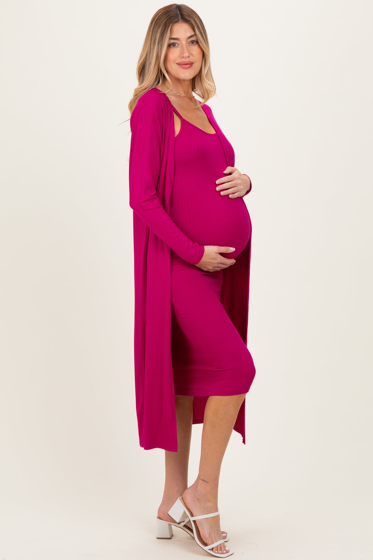 woman wearing a fuchsia maternity dress with a matching long cardigan and holding her baby bump