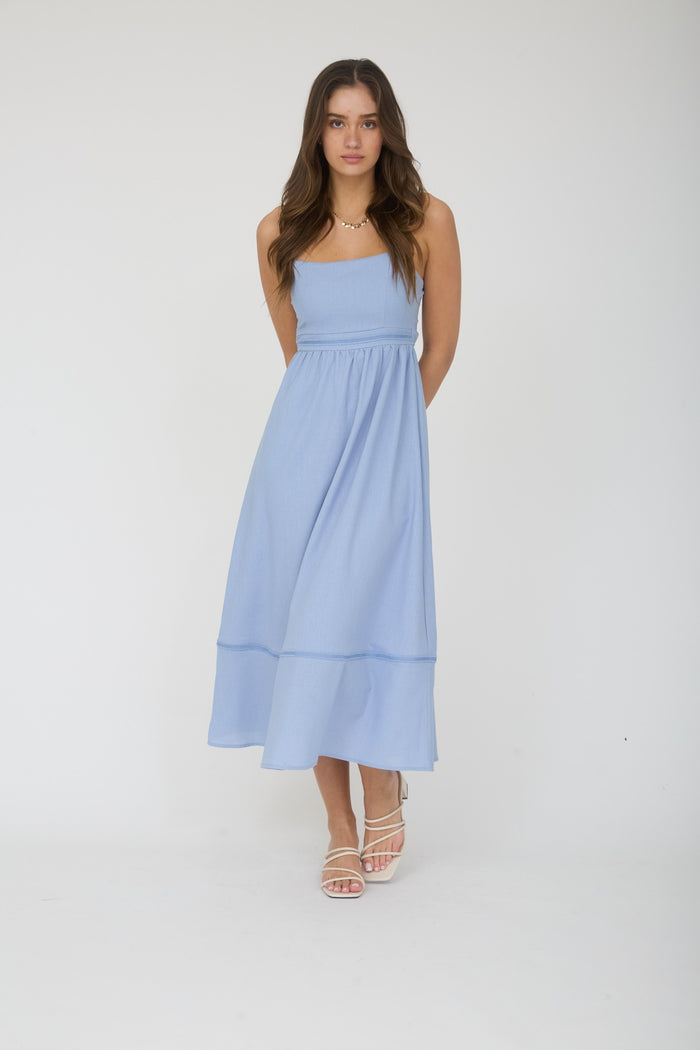woman wearing a light blue, sleeveless maxi dress with a fitted bodice and flowy bottom