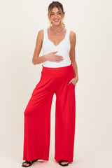 woman wearing a white sleeveless maternity top and red wide-leg maternity pants, holding her baby bump