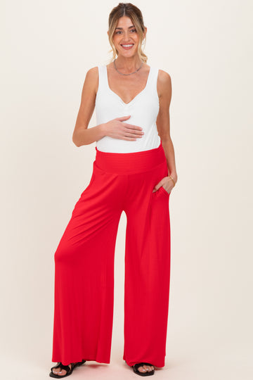 woman wearing a white sleeveless maternity top and red wide-leg maternity pants, holding her baby bump
