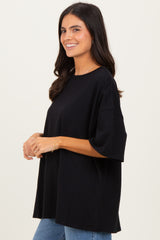 woman wearing a black oversized t-shirt paired with blue jeans, smiling and posing sideways