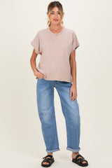 woman wearing a light beige maternity top and relaxed fit blue jeans, standing with one hand on her hip