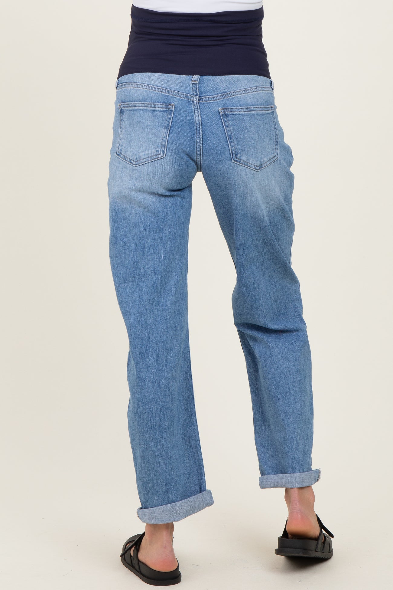 woman wearing light blue maternity jeans with a dark waistband, seen from the back, with a relaxed fit and rolled cuffs