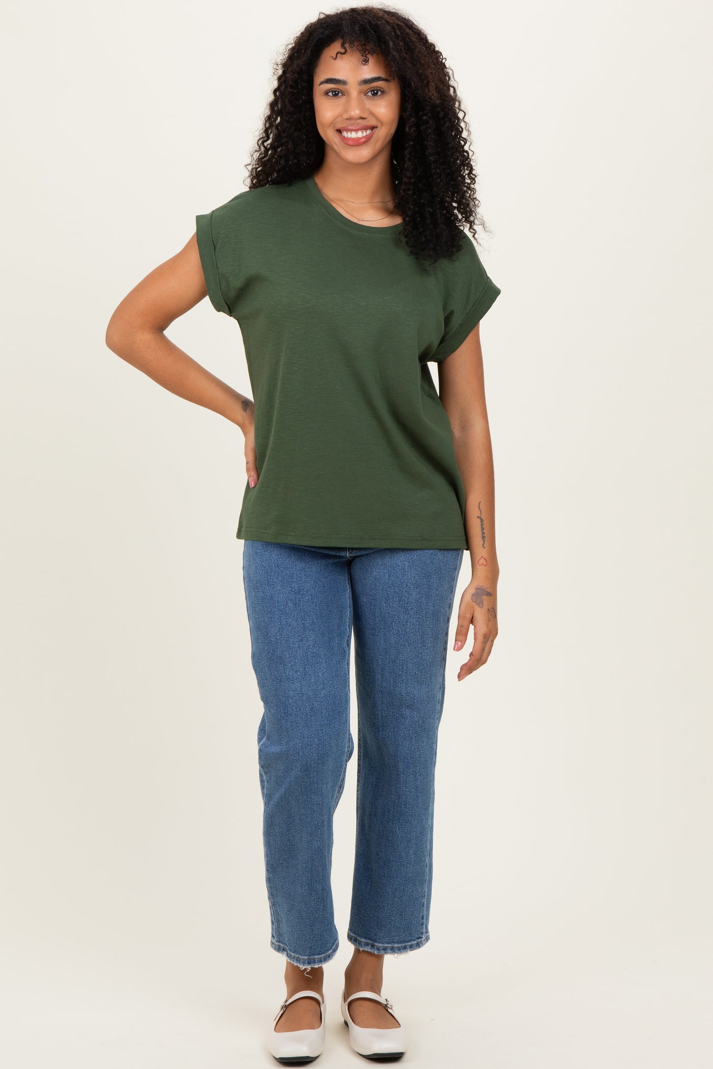woman wearing an olive green short sleeve top and light blue straight leg jeans, standing in a neutral background
