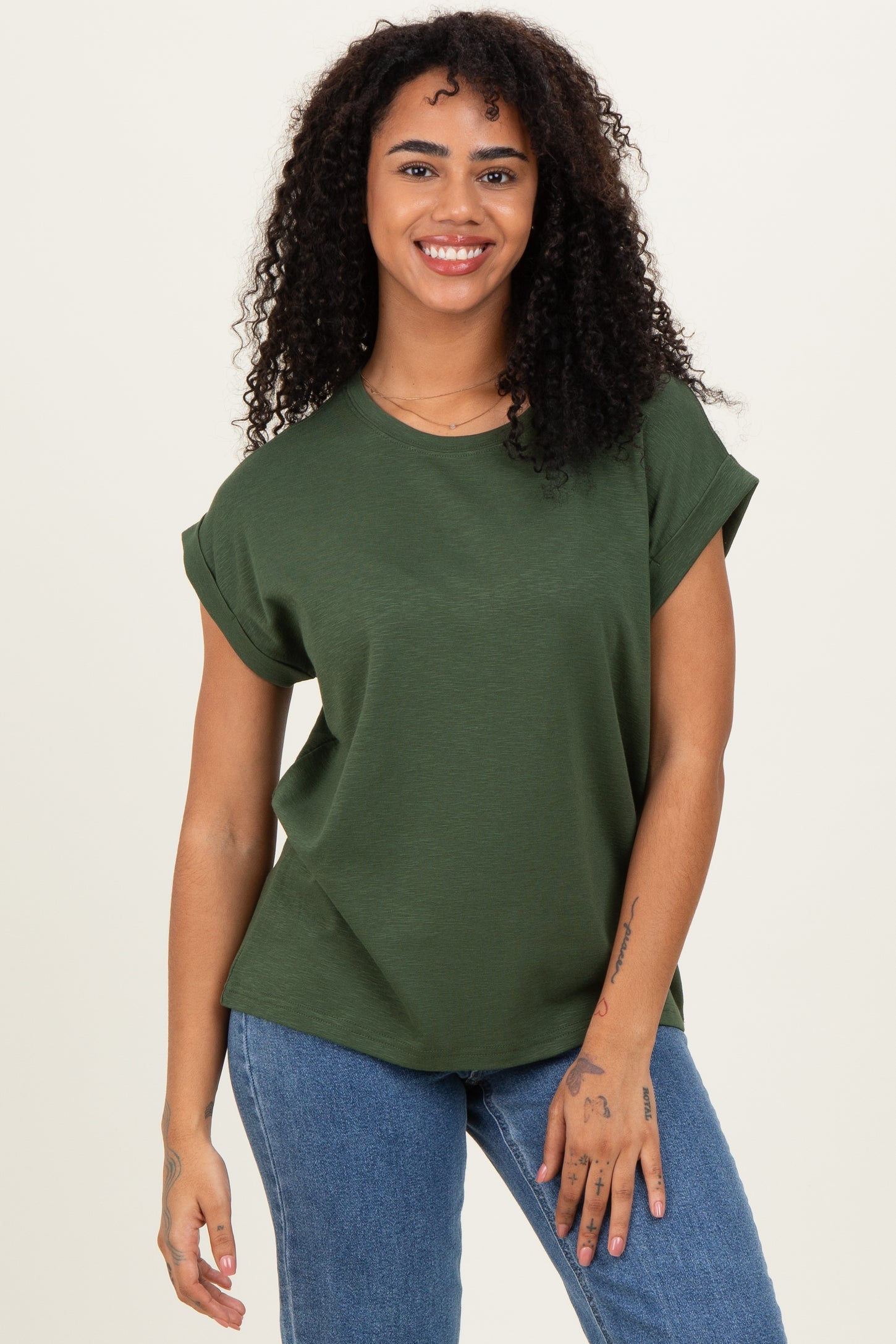 woman wearing a dark green short sleeve top and blue jeans, smiling at the camera