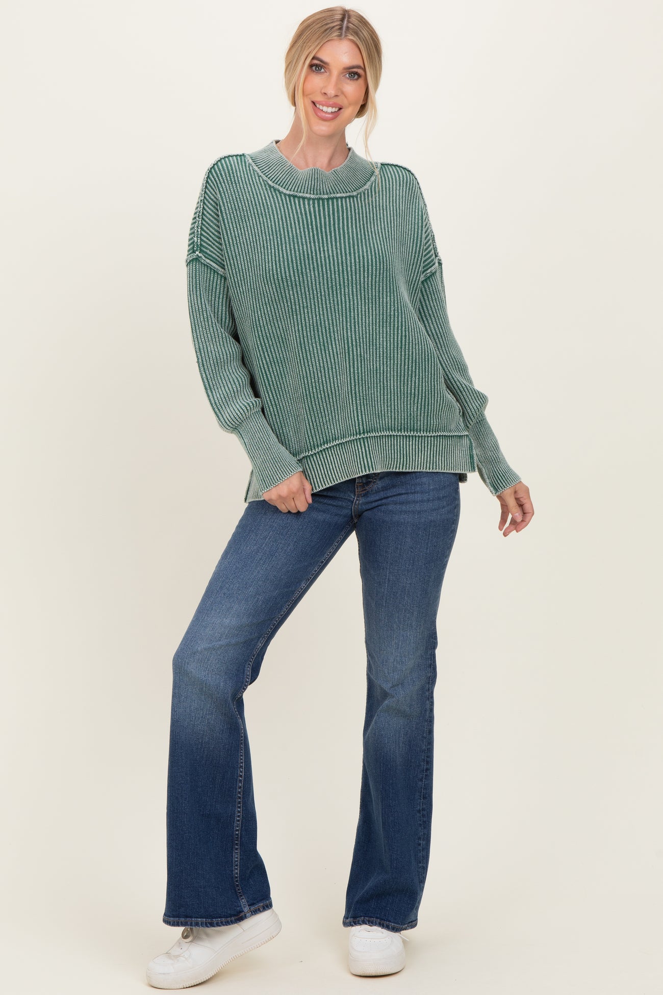 woman wearing a green striped oversized sweater and flared jeans with white sneakers