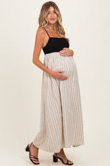 woman wearing a black maternity tank top and a beige striped maxi dress, holding her baby bump