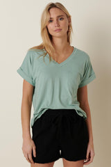 woman wearing a light green v-neck t-shirt with rolled sleeves and a pocket, paired with black drawstring shorts
