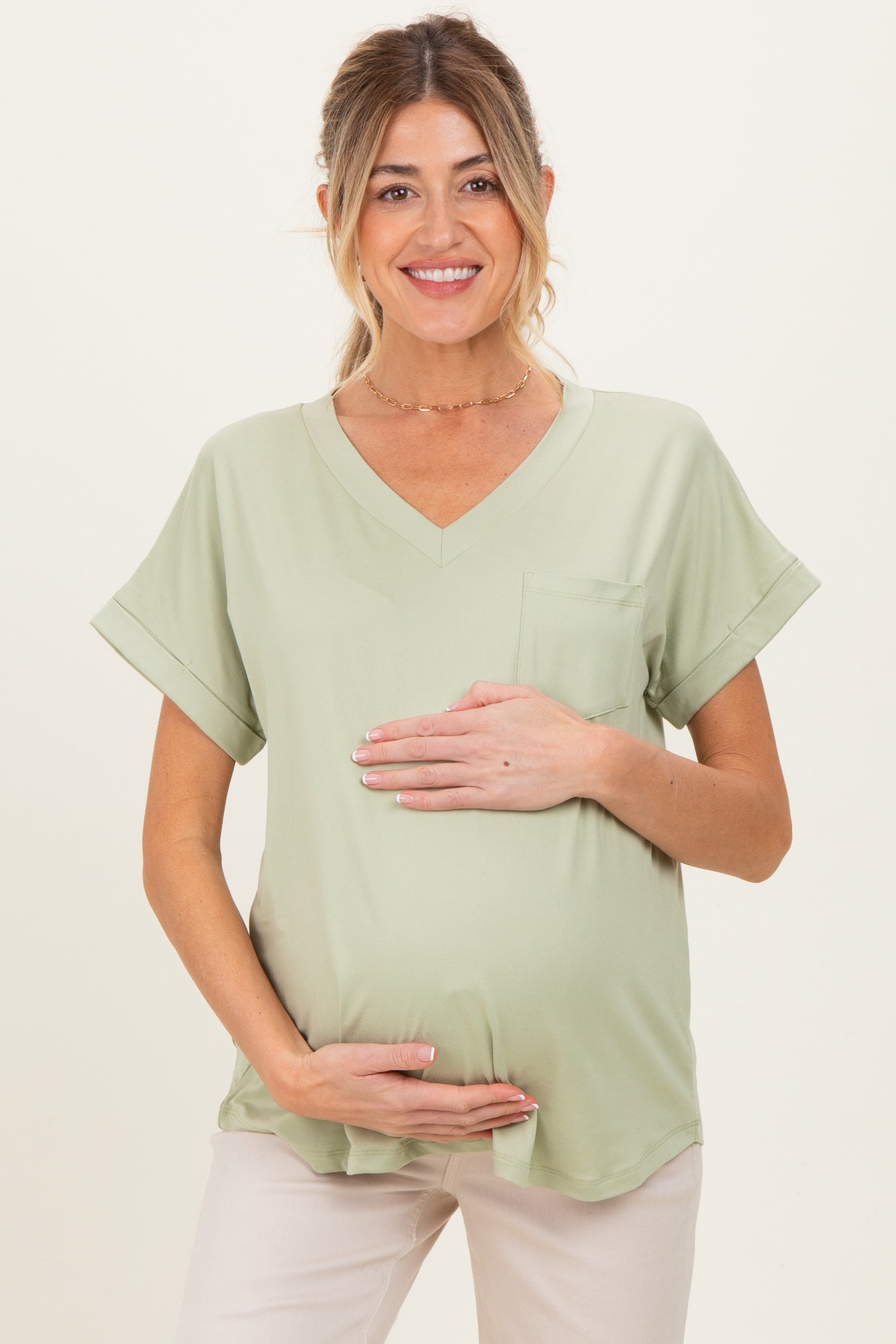 woman wearing a light green maternity top with a pocket and holding her baby bump