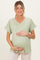 woman wearing a light green maternity top with a pocket and holding her baby bump